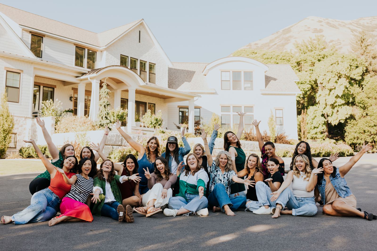 A big group of smiling women investors with their arms up in front of a white house